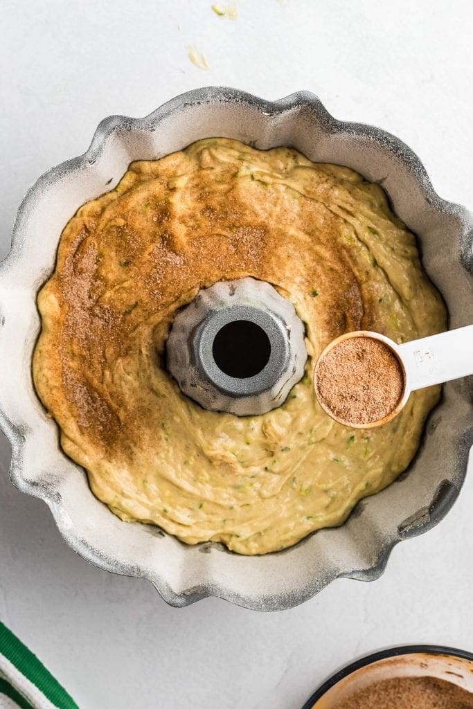 Teaspoon sprinkling cinnamon sugar over batter in bundt cake.