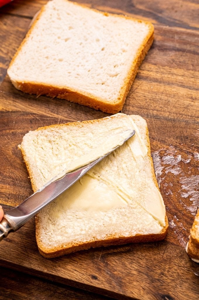 Butter knife spreading butter on a piece of bread on a wood cutting board.