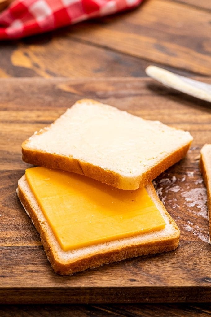 Slice of bread with a slice of cheese on top and another slice of bread half on the cheese.