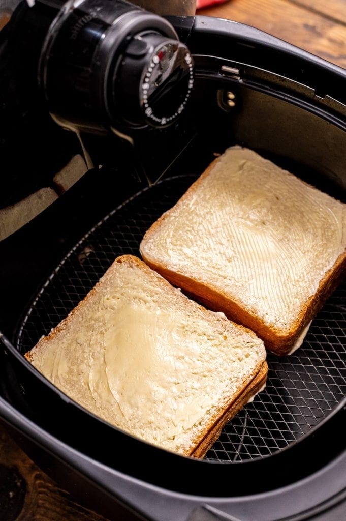 Two grilled cheese sandwiches in air fryer before cooking.