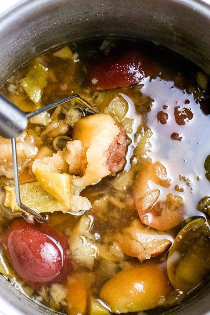 Stock pot with cooked ingredients with a masher mashing them together.