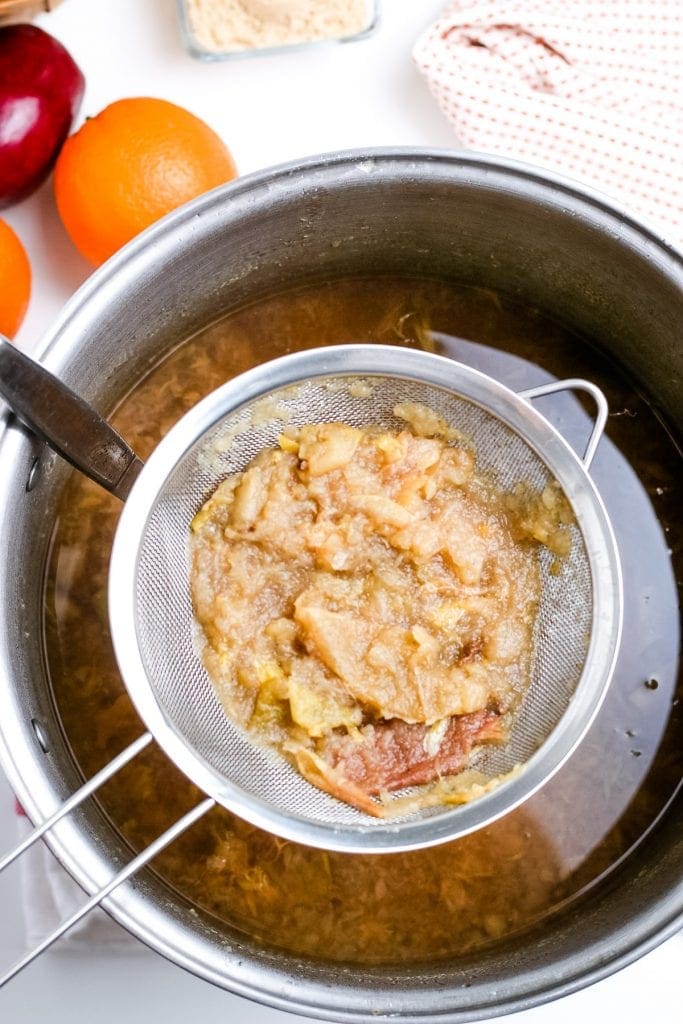 Mesh strainer straining apple cider ingredients.