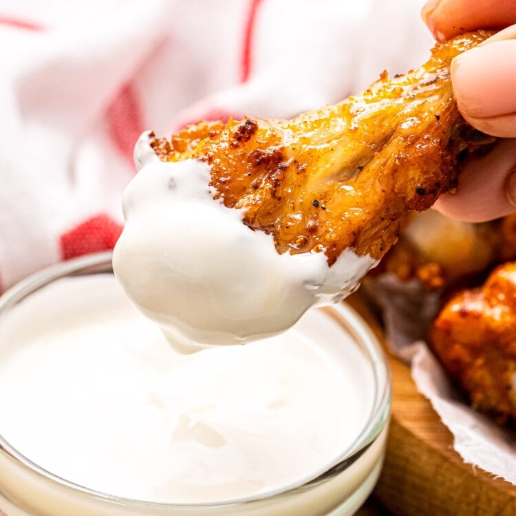 Hand holding chicken wing that is dipped in ranch