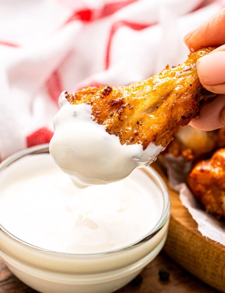 Hand holding chicken wing that is dipped in ranch