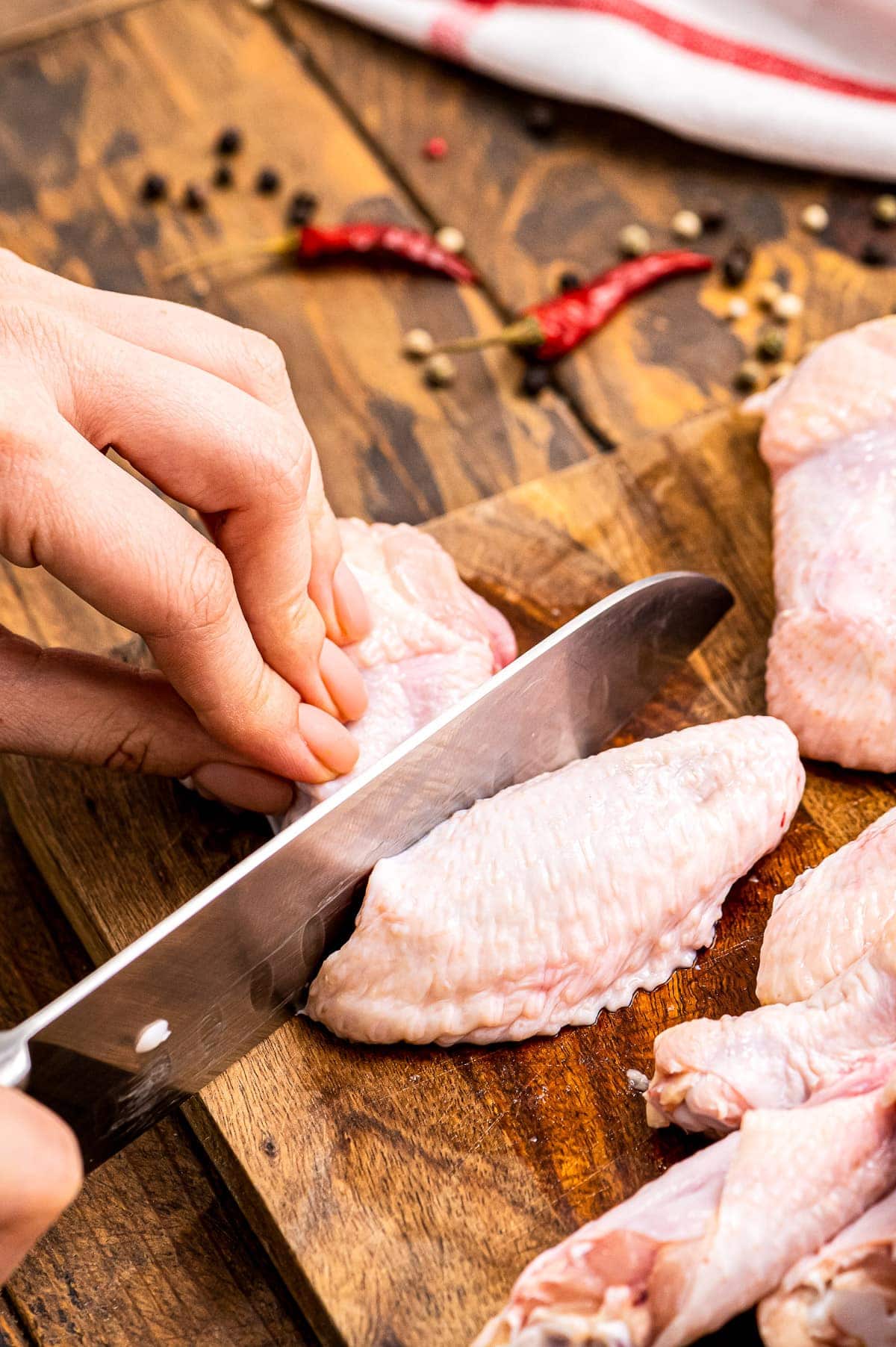 Cutting tip off of a chicken wing on a wood cutting board.