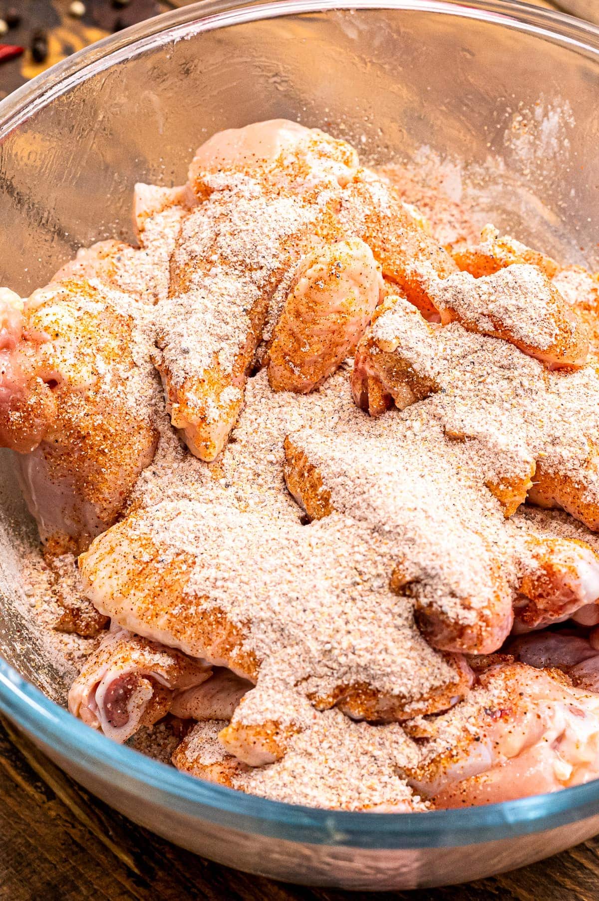 Glass bowl with chicken wings and spice rub on top of them before mixing.