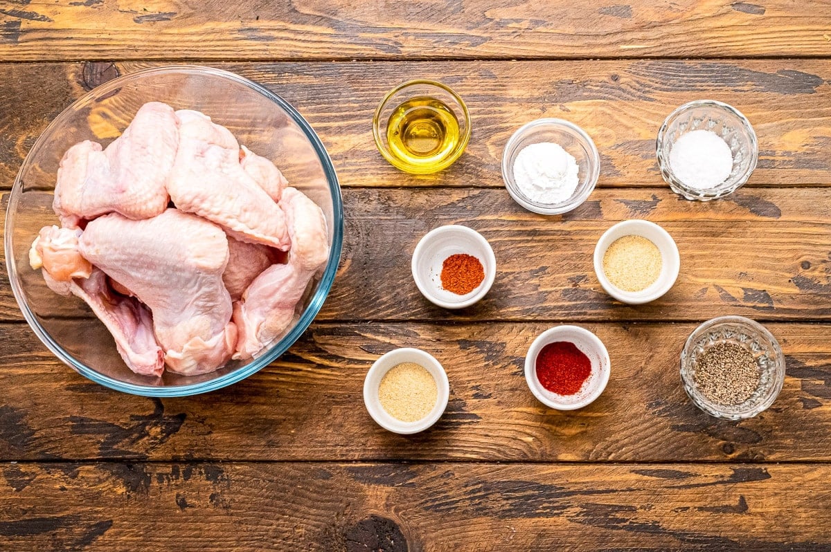 Overhead image of ingredients including a bowl of chicken wing, spices in bowl and oil in glass dishes.