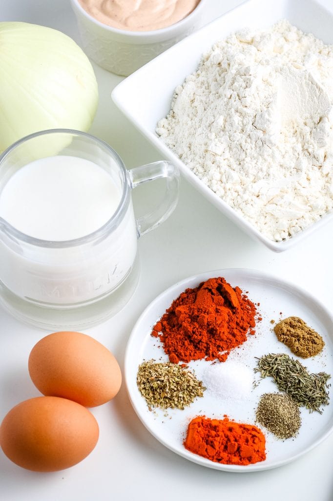 Overhead photo of ingredients needed to make Fried Blooming onion like spices, milk, eggs, flour, onion.