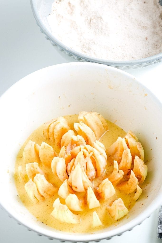 Cut and floured onion sitting in egg mixture in a white bowl.