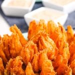 Close up photo of a blooming onion with small square dishes of dipping sauce in background