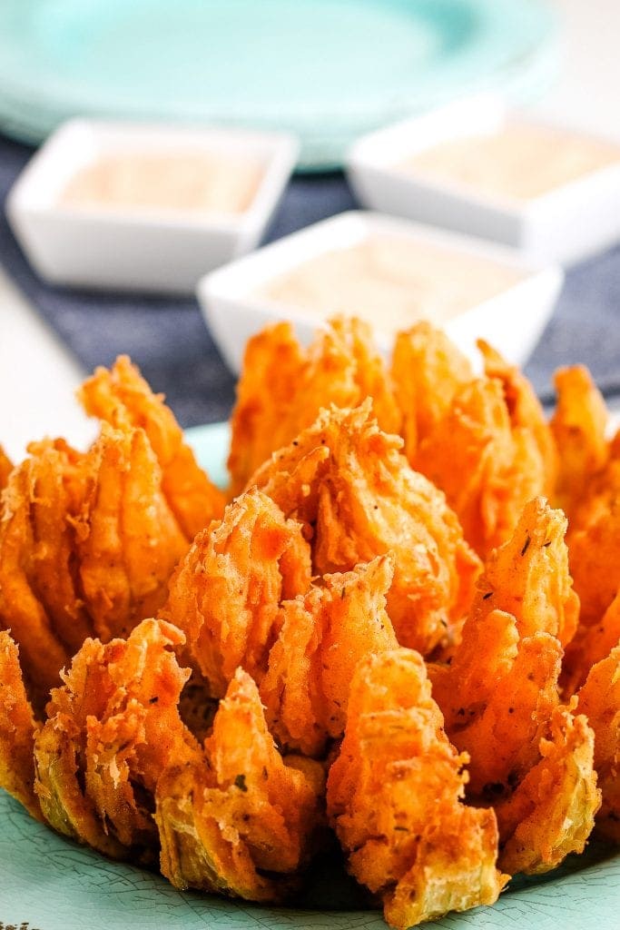 Close up photo of a blooming onion with small square dishes of dipping sauce in background
