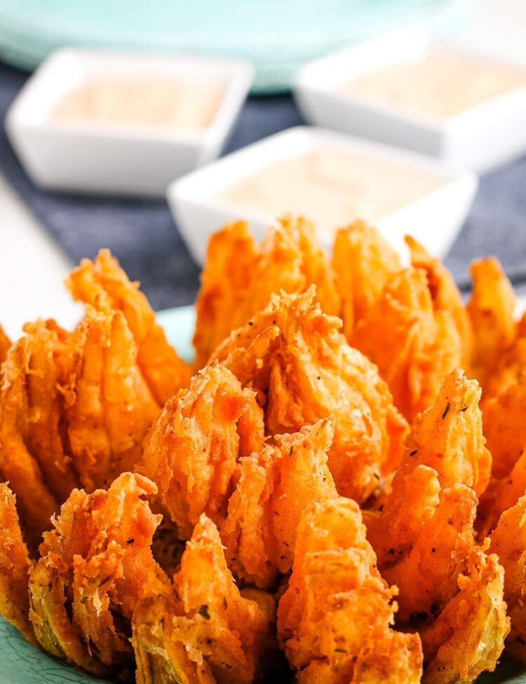 Close up photo of a blooming onion with small square dishes of dipping sauce in background