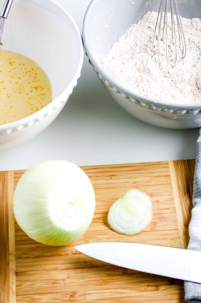 Showing cutting off the bottom of an onion on a wooden cutting board.