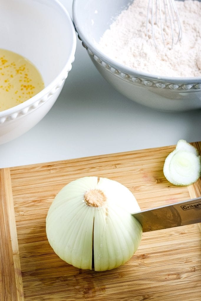 Making the first four cuts of the onion in quarters on a wooden cutting board.