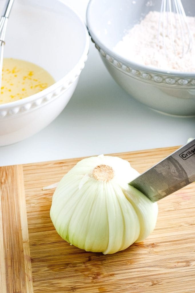Slicing smaller cuts into the onion with knife on wood cutting board.