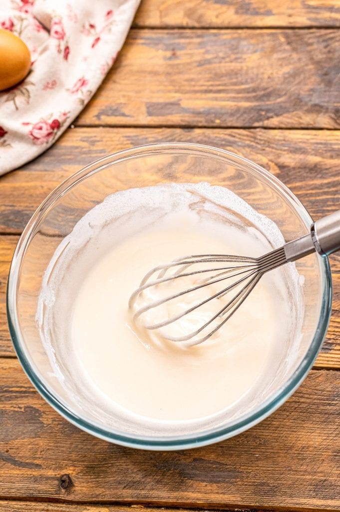 Glass bowl of powdered sugar icing with whisk in it