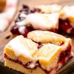 A sliced piece of Cherry Pie Bars on a wooden cutting board with another behind it.