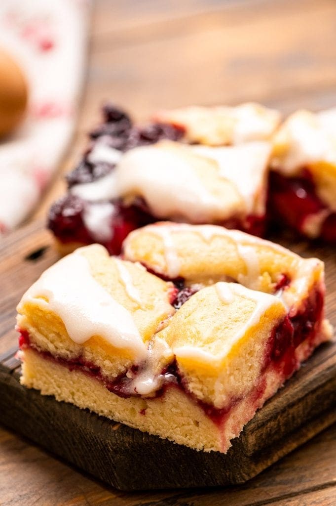 A sliced piece of Cherry Pie Bars on a wooden cutting board with another behind it.