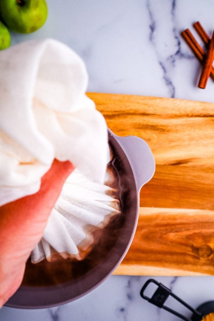 Hand holding cheesecloth to drain off apple cider.