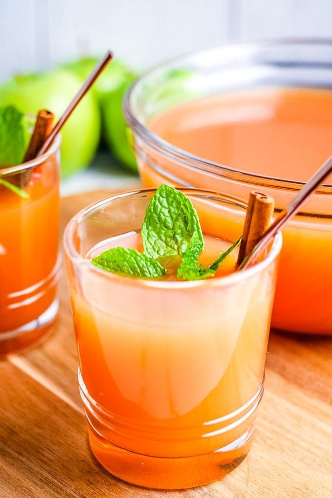 Glass of Instant Pot Apple Cider with a bowl of it in background sitting on wooden background.