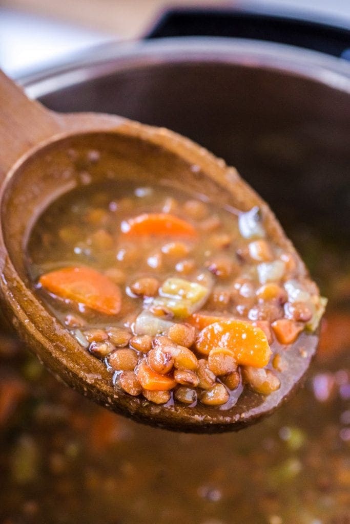 Wooden spoon with a scoop of lentil soup on it.