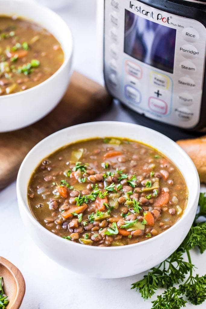 White bowl with Pressure Cooker Lentil Soup in it and a pressure cooker in background.