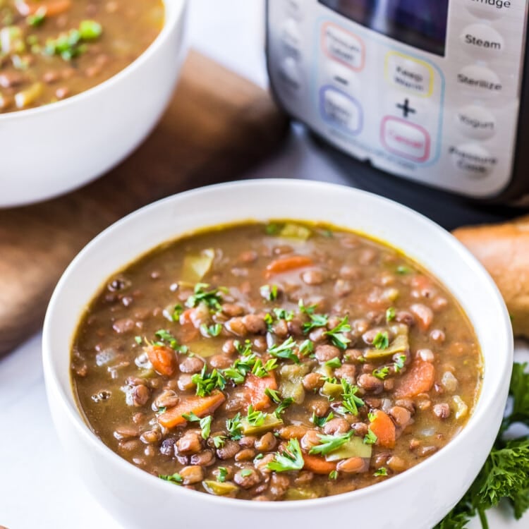 White bowl with Pressure Cooker Lentil Soup in it and a pressure cooker in background.