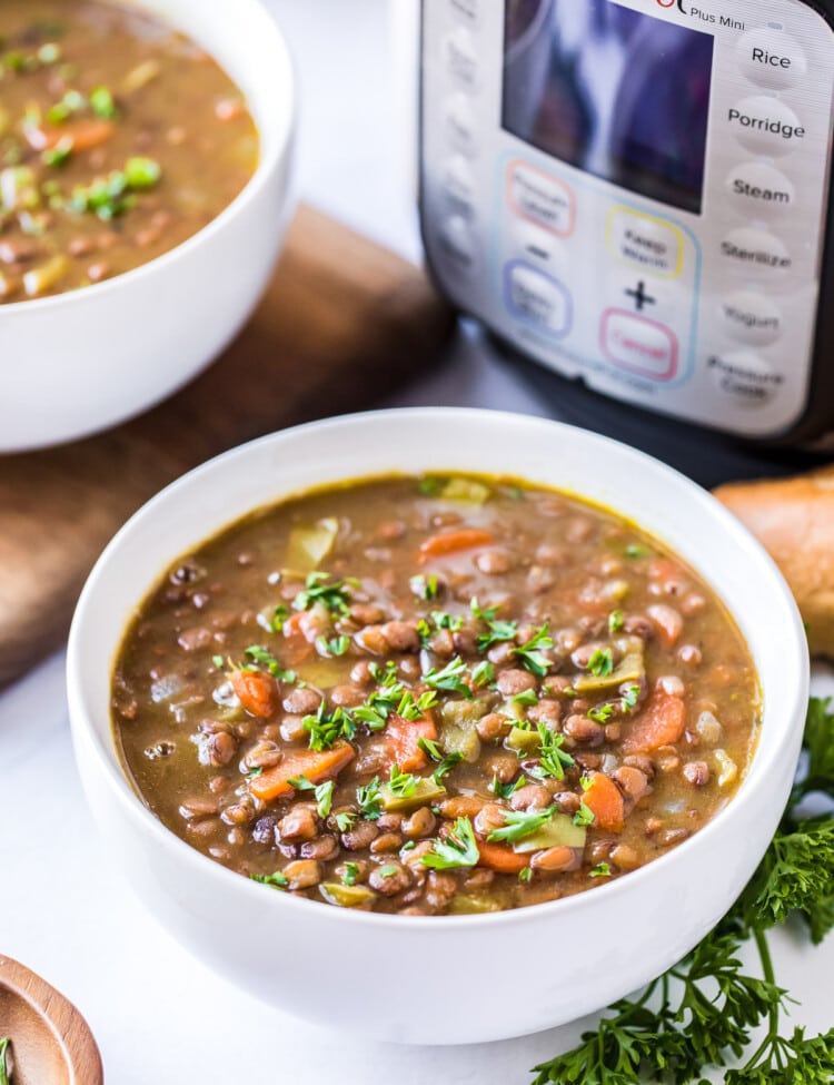 White bowl with Pressure Cooker Lentil Soup in it and a pressure cooker in background.