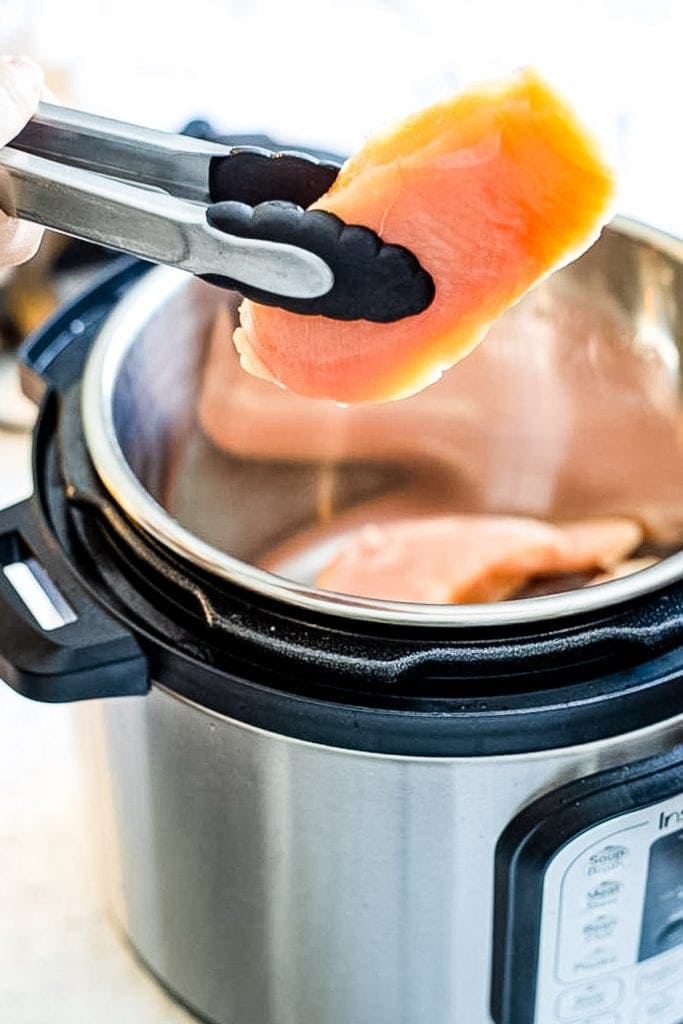 Tongs putting boneless chicken breast into Instant Pot