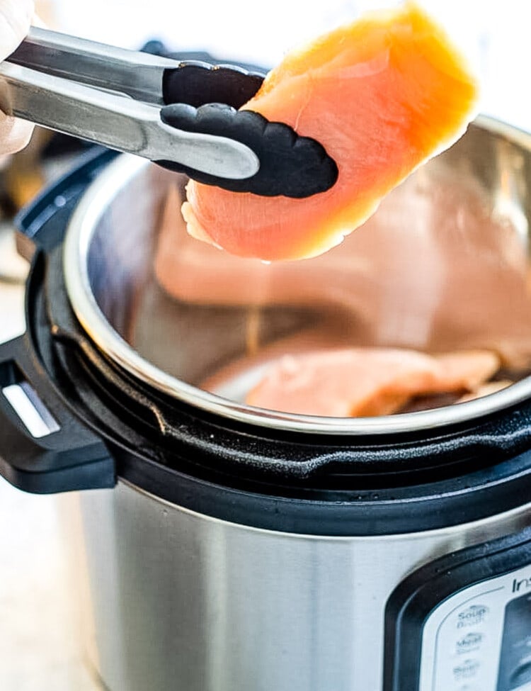 Tongs putting boneless chicken breast into Instant Pot