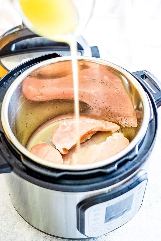 Pouring chicken broth into an Instant Pot with boneless chicken breasts.