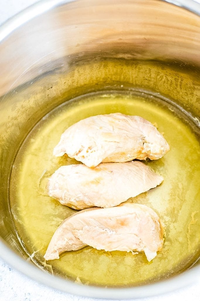 Instant Pot with cooked boneless chicken breasts in broth.