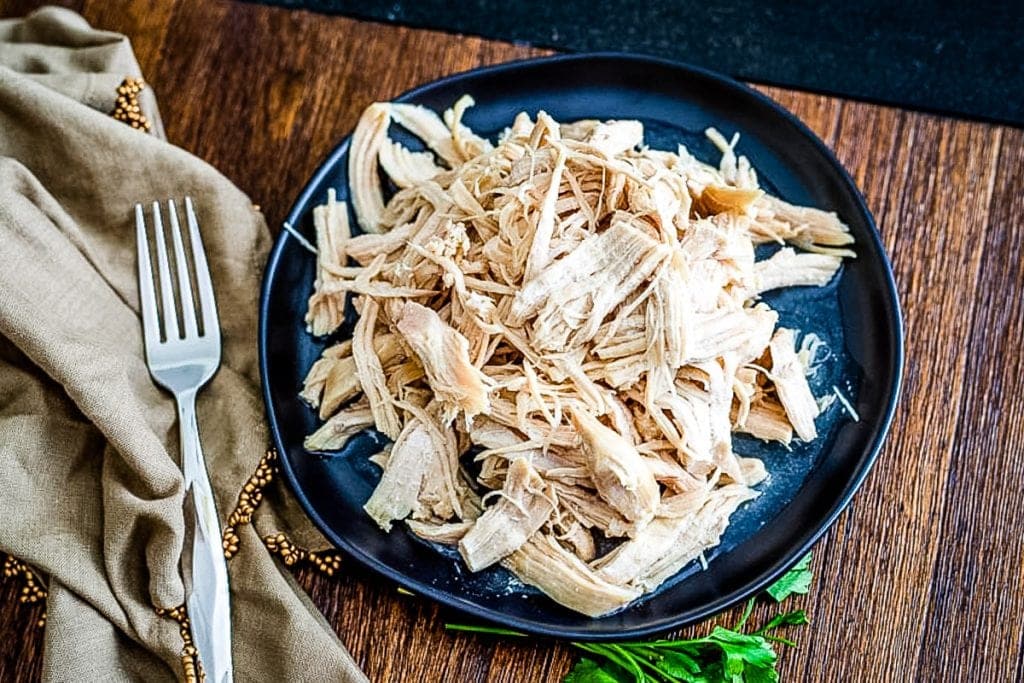 Overhead view of a plat of shredded chicken with a tan napkin with fork on top of it next to it.