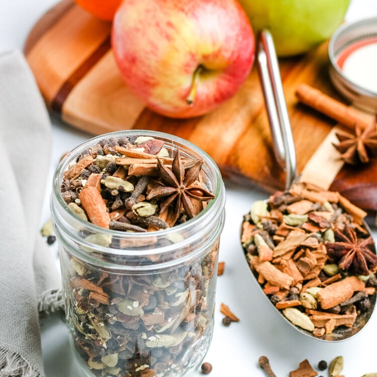 Mulling Spices in glass jar with apples behind it.