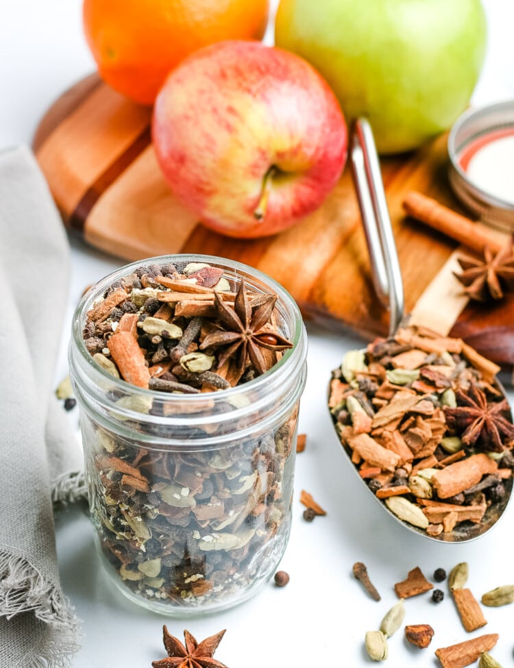 Mulling Spices in glass jar with apples behind it.