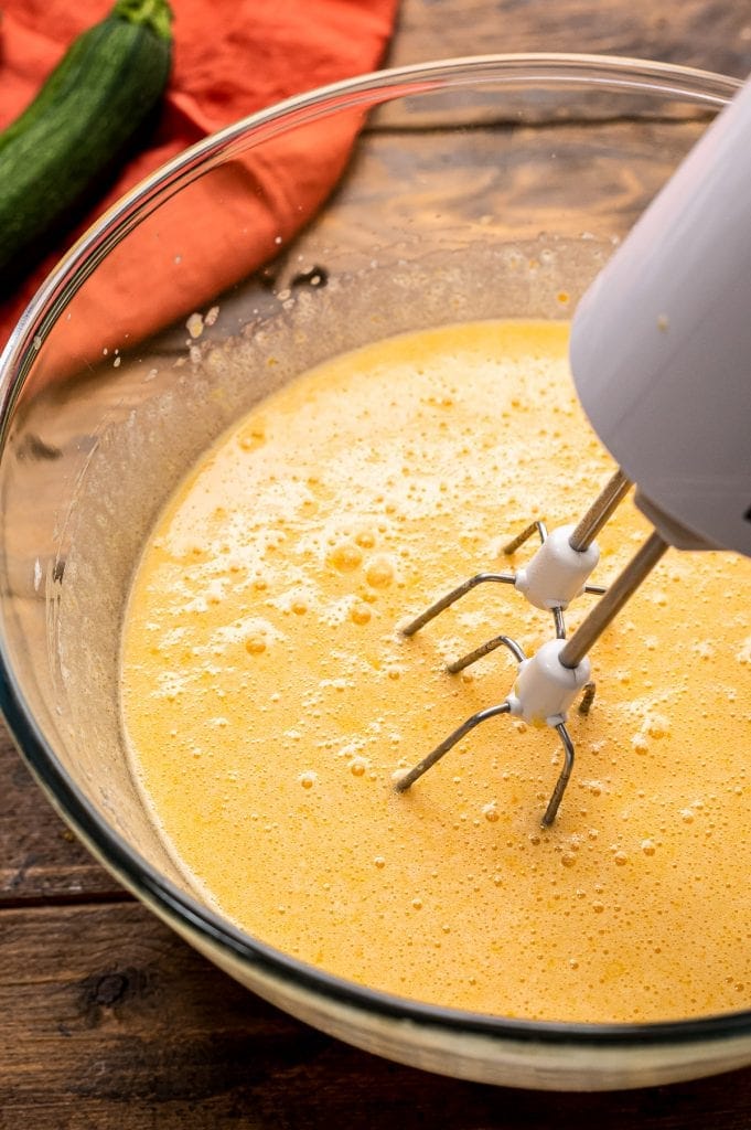 Hand mixer combine pumpkin bread ingredients in glass bowl.