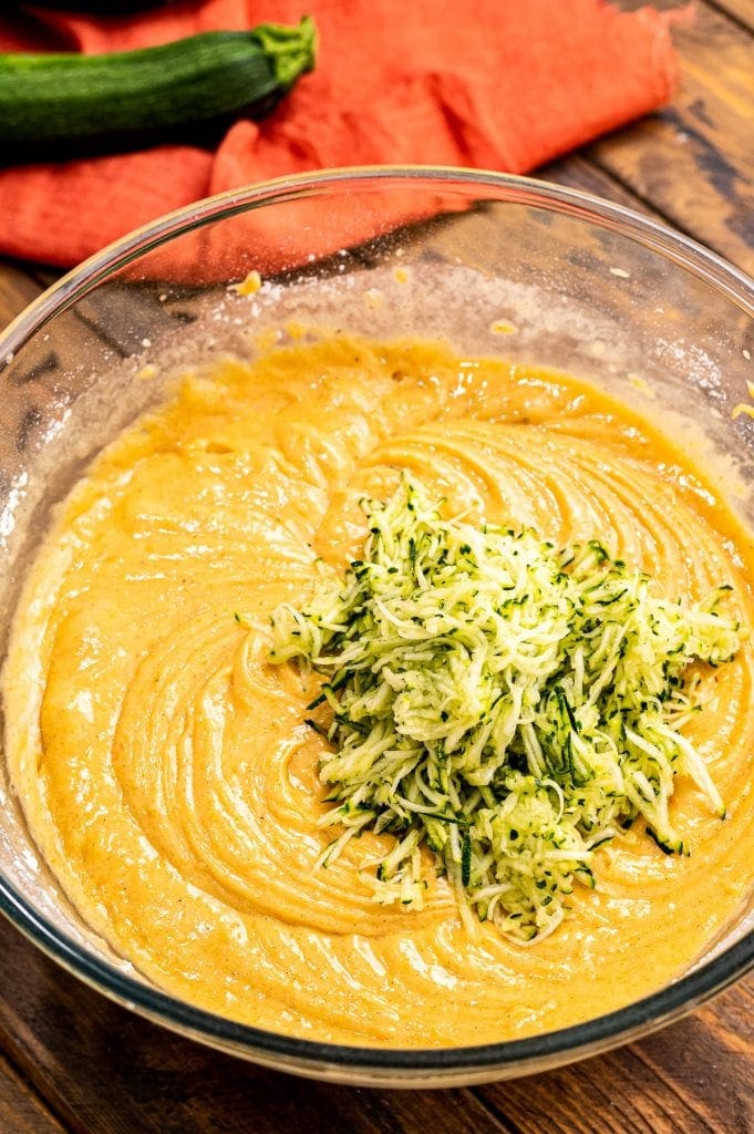 Shredded zucchini being added to pumpkin bread batter.