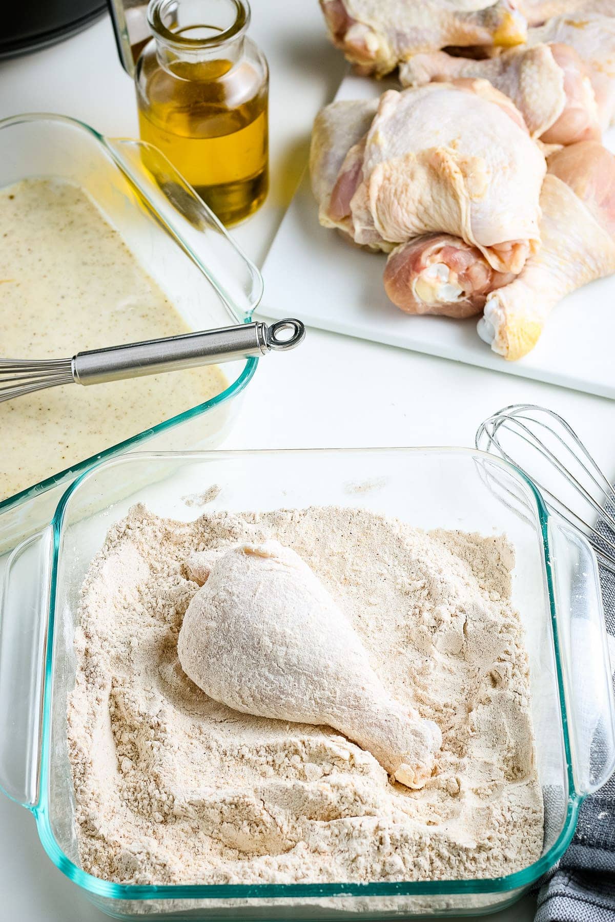 Chicken Leg in coated in a square dish with more coating in it.