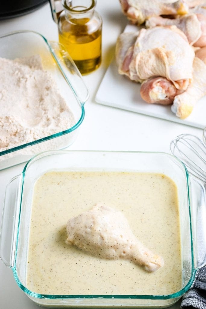 Chicken Leg laying in buttermilk batter in glass square baking dish.