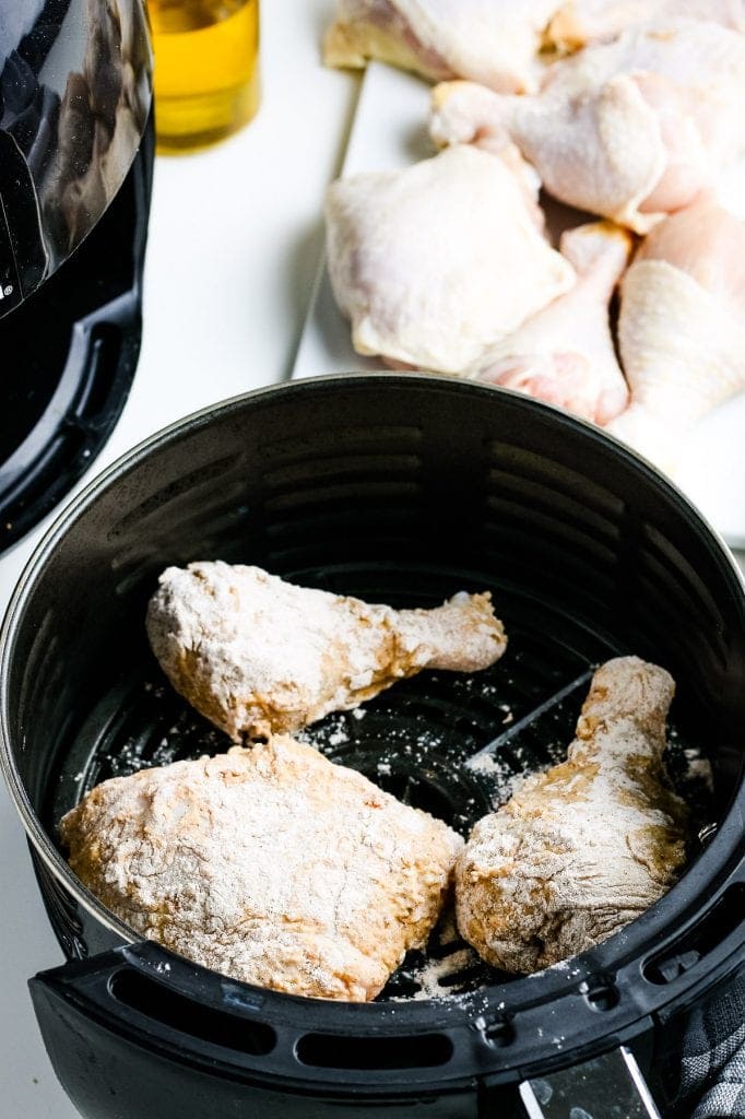 Three pieces of battered chicken in black air fryer basket before frying.