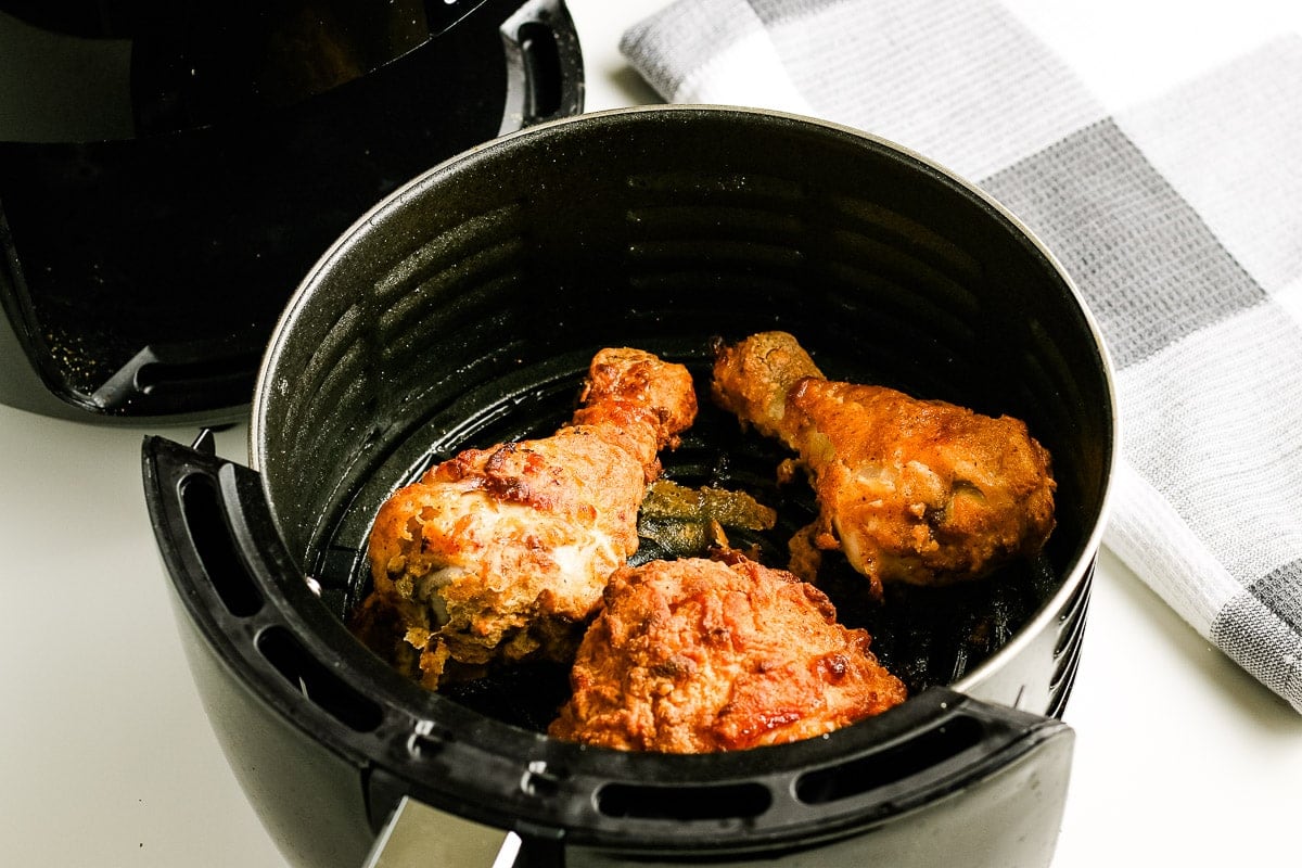 Fried Chicken that is cooked in black round air fryer basket.