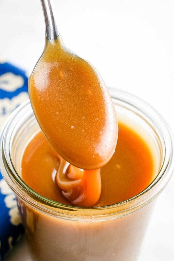 Caramel Sauce on spoon drizzling into jar of sauce.