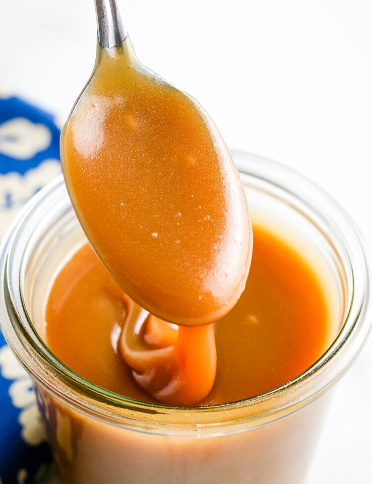 Caramel Sauce on spoon drizzling into jar of sauce.