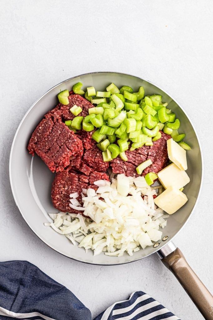 Skillet with hamburger, celery, onions and butter in it before cooking.