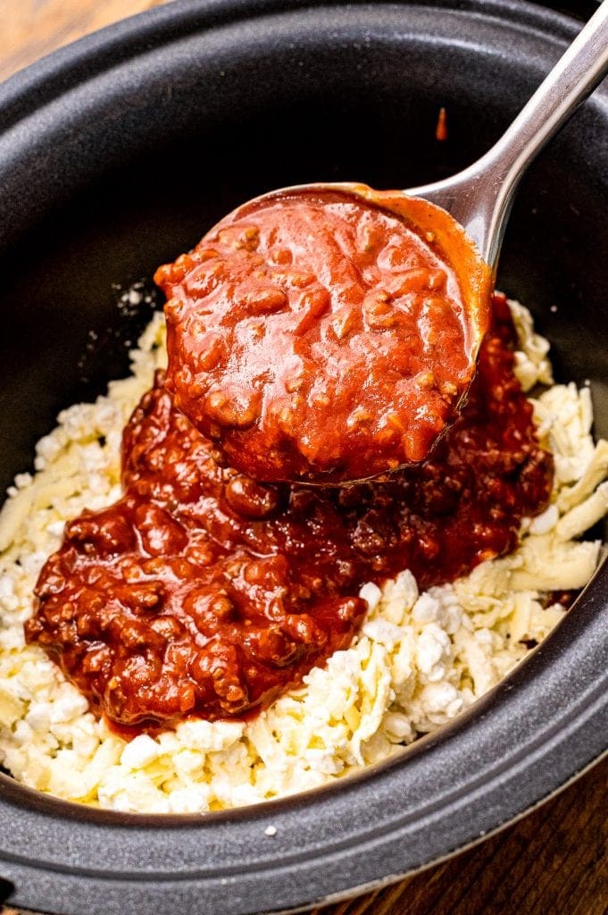 Spoon ladling meat sauce on top of cheese in crock pot