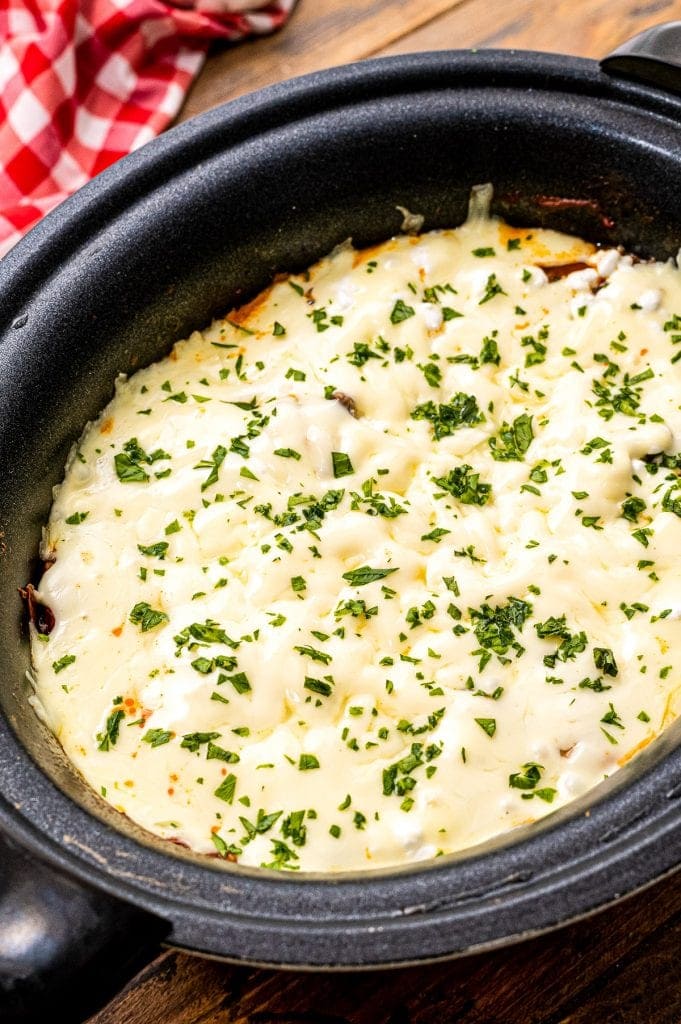 Crock Pot with cooked lasagna in it garnished with chopped parsley