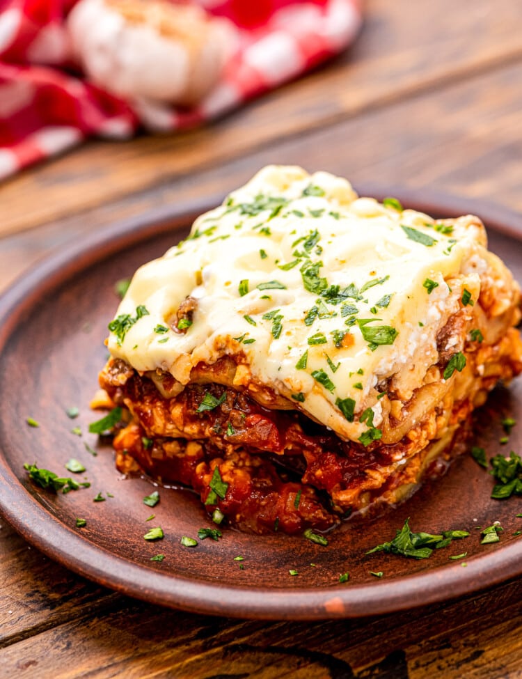 Small wooden plate with a piece of lasagna on it garnished with parsley on wooden background.