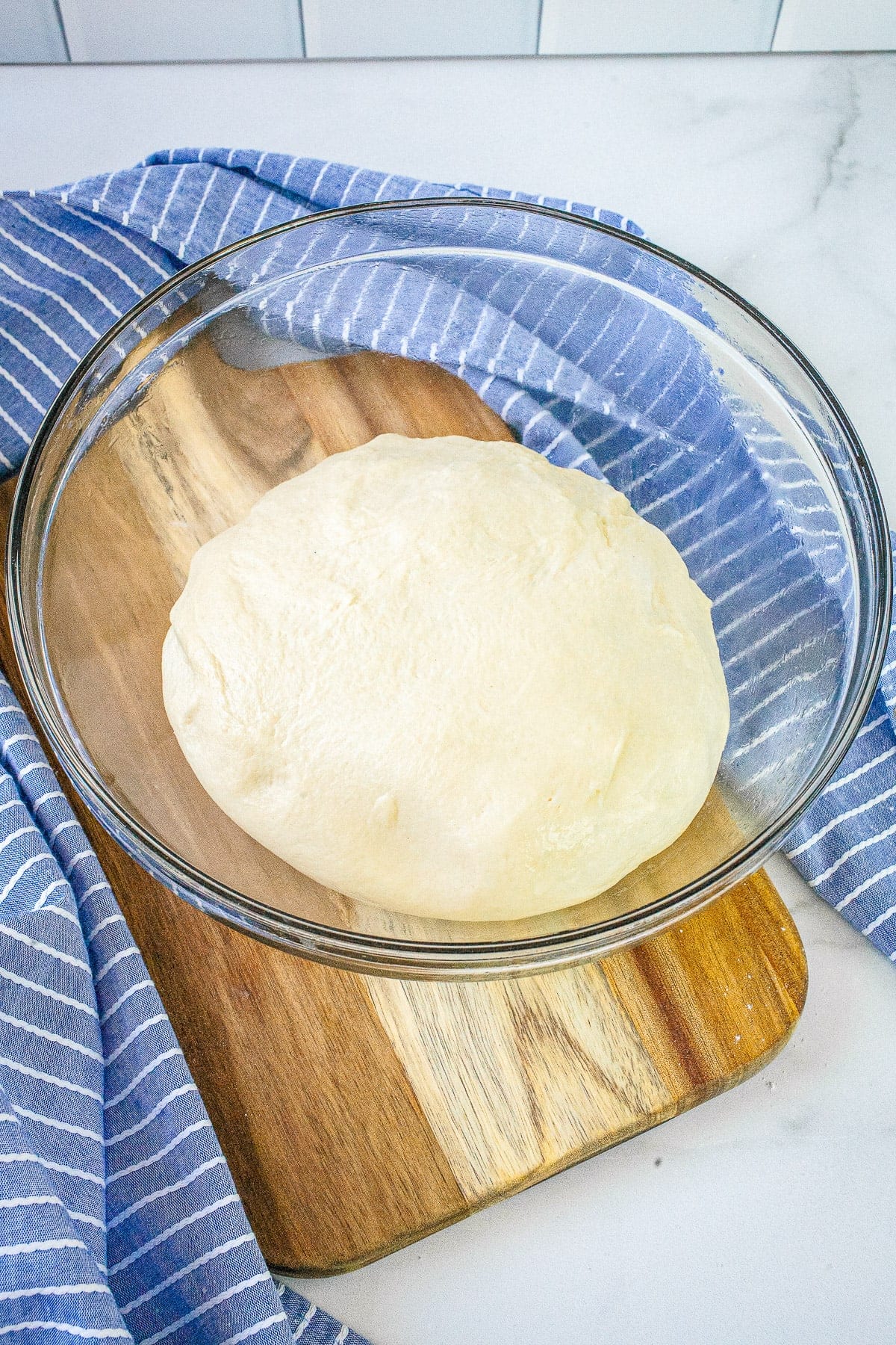Glass bowl with dinner roll dough in it before rising.
