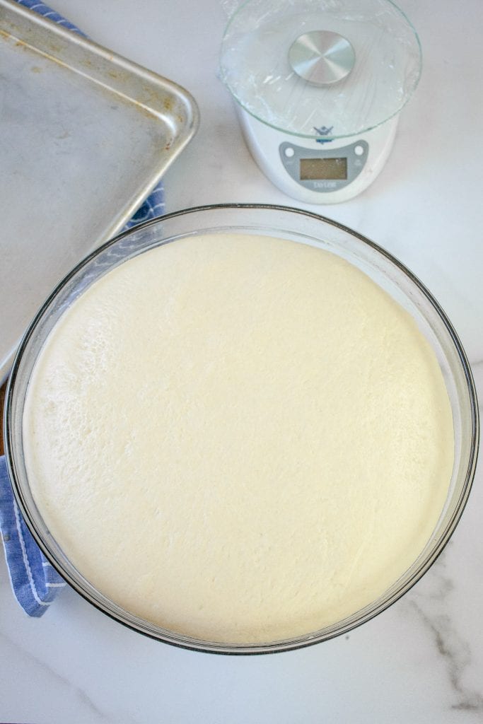 An overhead image of a glass bowl with raised dinner roll dough in it.