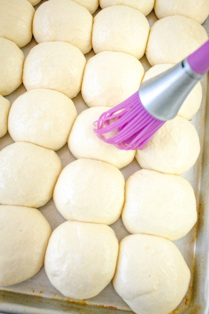 Silcone brush that is brushing butter onto dinner roll dough balls.